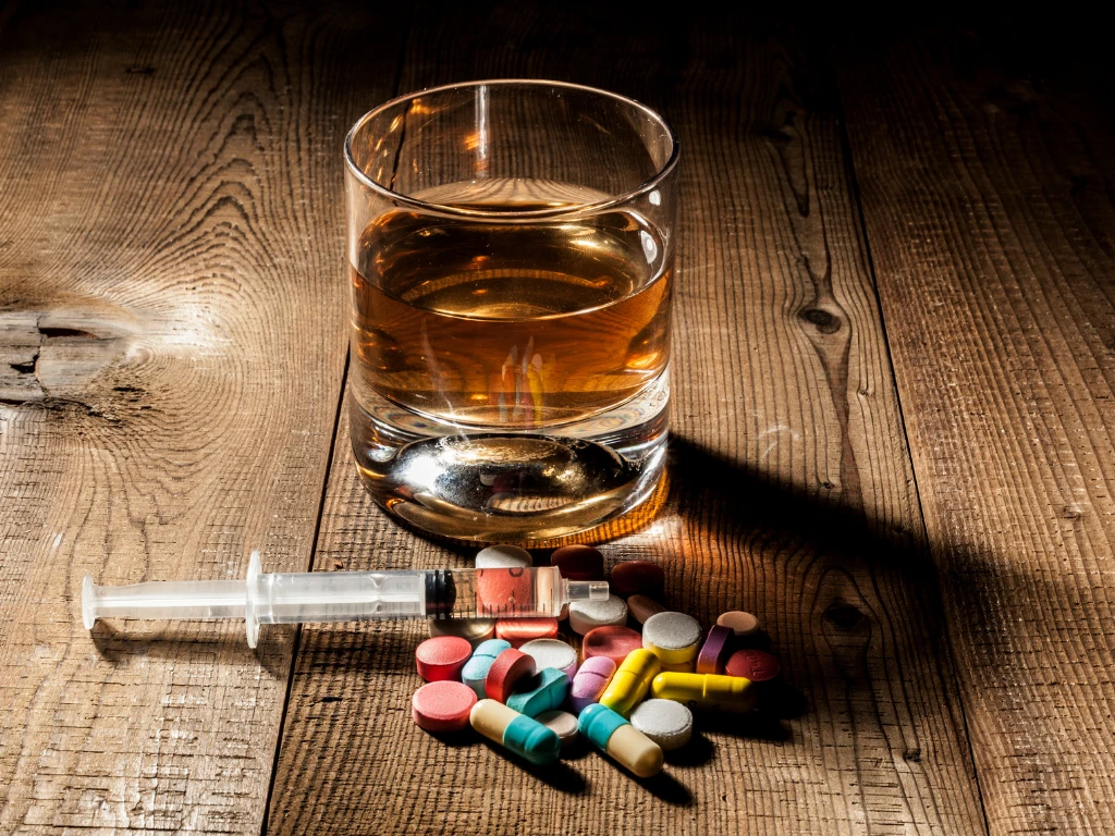 Alcohol, pills, and syringe on wood