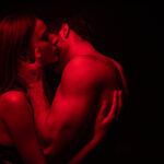 side view of passionate undressed sexy young couple kissing in red light isolated on black